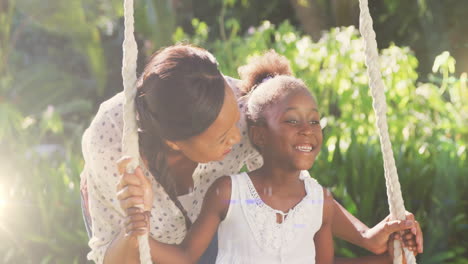 spot of light against african american pushing her daughter on the swing in the garden