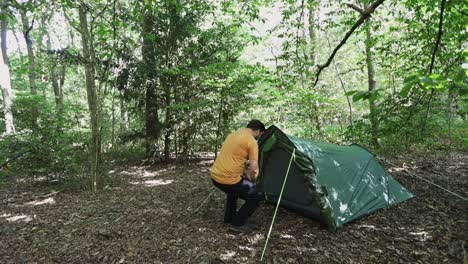 lonely camper walking into his tent in dense woodland area, follow up view