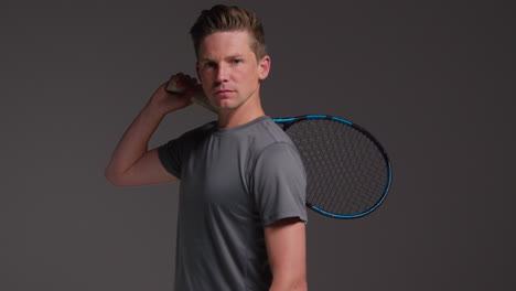 Studio-Portrait-Of-Male-Tennis-Player-Holding-Racket-Shot-Against-Grey-Background