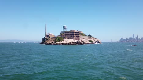 toma en movimiento del cardán acercándose a la parte trasera de la isla de alcatraz en barco con el puente de la bahía y san francisco visibles en el fondo