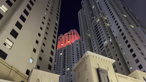 wide view from the ground of a tall tower with red lights at the top in dubai city at night