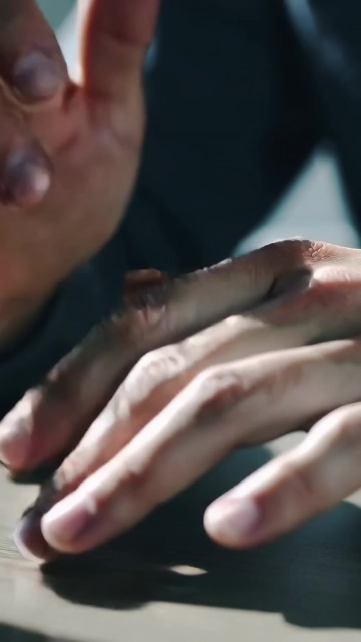 Vertical video: Red dot appearing, resting adult hands in dark sleeves tapping and rubbing on table