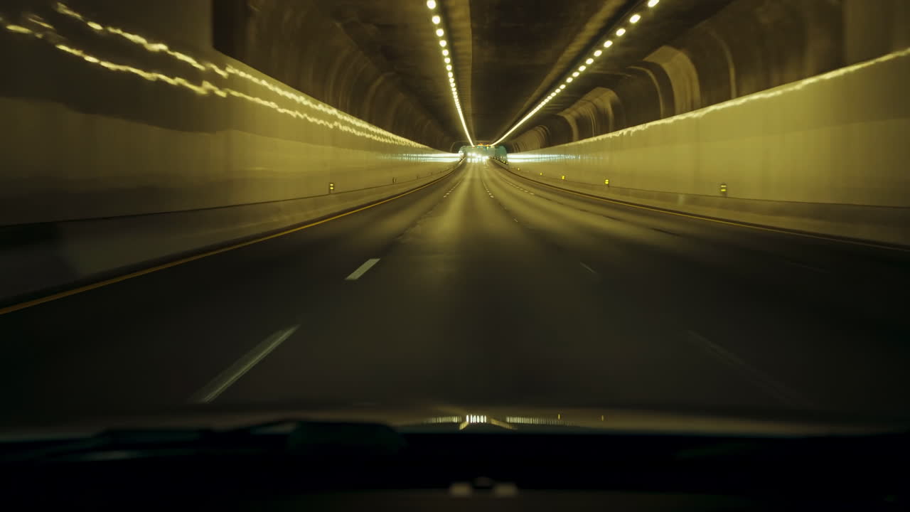 Tunnel autostradale notturno con luci che illuminano la strada, movimento fluido in avanti dall'abitacolo del veicolo, lampade gialle calde.