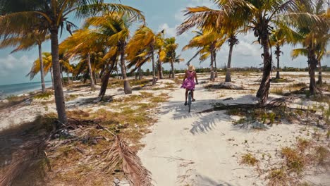 a female riding a bike along a beach, under palm trees on a sunny day, in caye caulker, belize