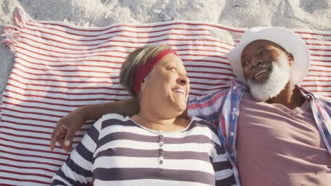 happy senior african american couple lying on blanket at beach, slow motion