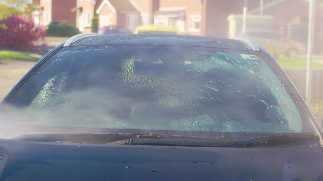 Rinsing windscreen on a black car with protection and instant water sheeting and beading