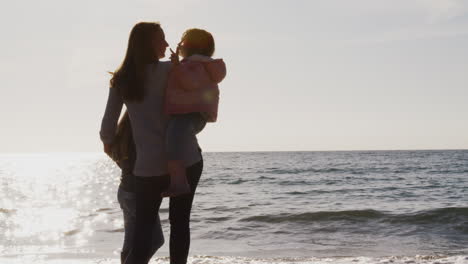 rear view of mother with daughters looking out to sea silhouetted against sun