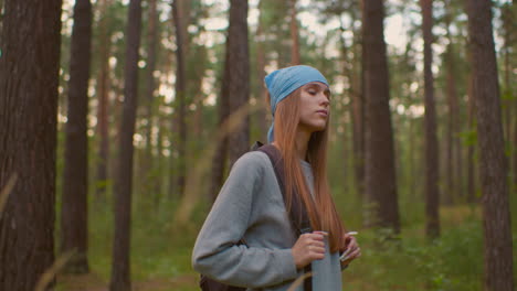 young girl in forest holding backpack straps, gazing contemplatively with serene surroundings, long hair cascading over shoulders, blue bandana and soft expression