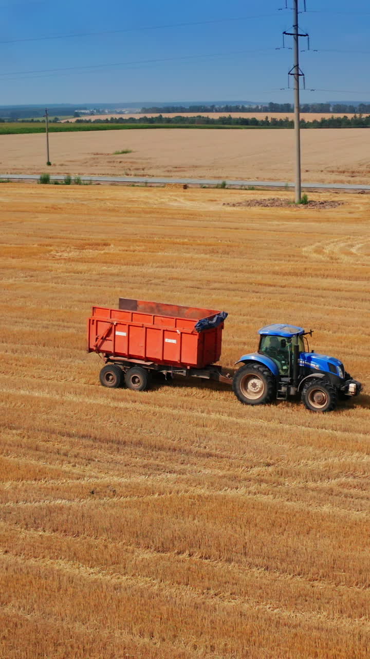 Tractor machines moving by the agricultural plantation. Truck being uploaded with the hay bales at the background. Vertical video