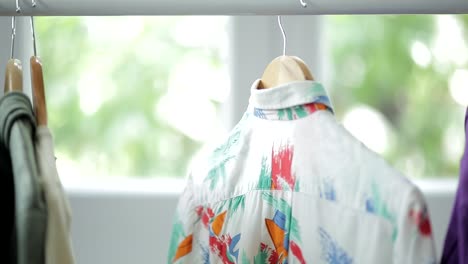 close up of young boy sliding away shirts from coat rack and choosing from them