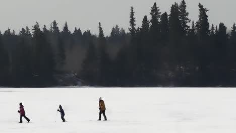 Familia-De-Esquiadores-De-Fondo-Esquiando-En-Un-Lago-Congelado-En-Invierno-Durante-Una-Tarde-Crepuscular-En-Un-Día-Frío-Mientras-Un-Dron-De-Grado-Profesional-Vuela-A-Su-Alrededor-En-Un-Estilo-De-Video-De-Punto-De-Interés