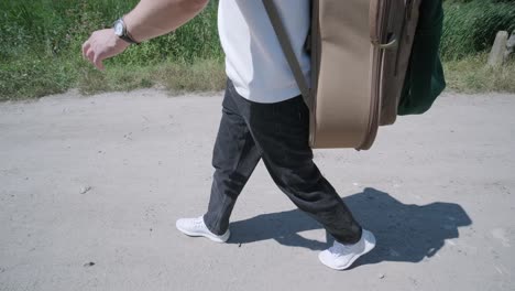 young man walking with guitar on street near forest