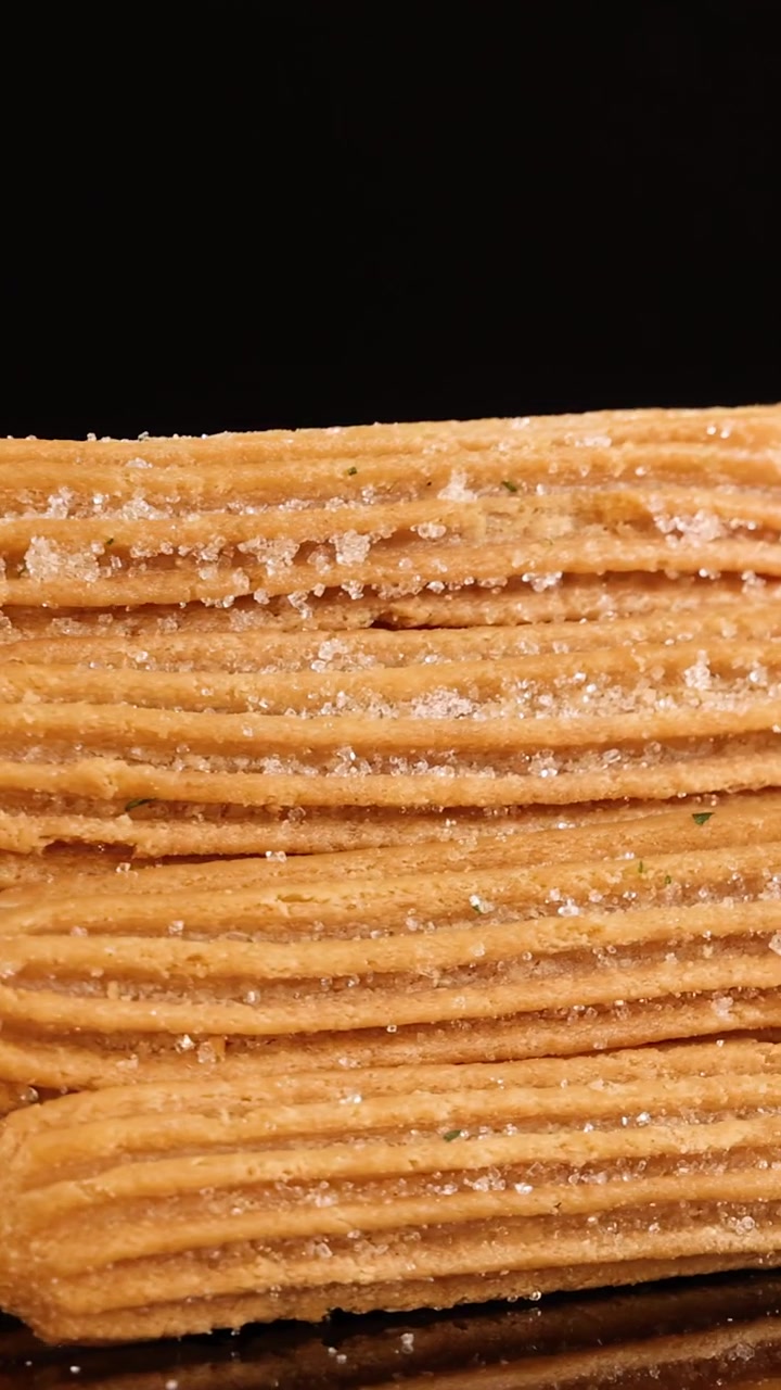 Una pila ordinata di churros cosparsi di zucchero ruota dolcemente su uno sfondo nero lucido, illuminata da una luce da studio uniforme e riprese ravvicinate.