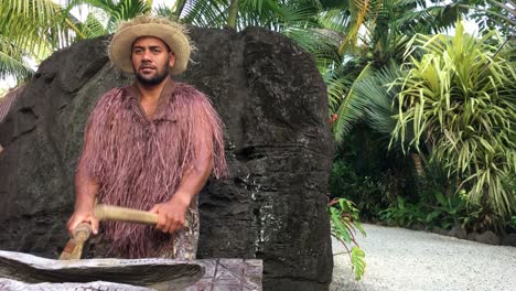 pacific islander man plays on a large wooden log pate drum