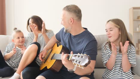 dad man playing guitar for his family while sitting on sofa. relaxing at home on the sofa, the husband sings for his wife. happy family resting together at home