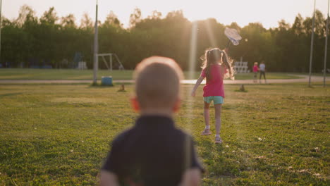 girl runs with hoop net boy stands on lawn on playground