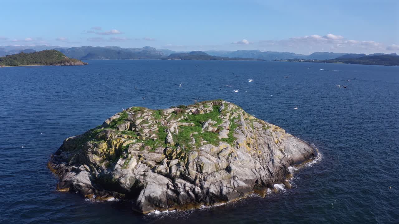 Island surrounded by ocean with scenic mountains in the distance, Norway