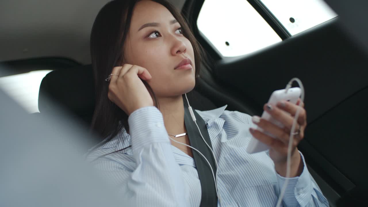 mujer asiática escuchando música en su teléfono inteligente en el coche