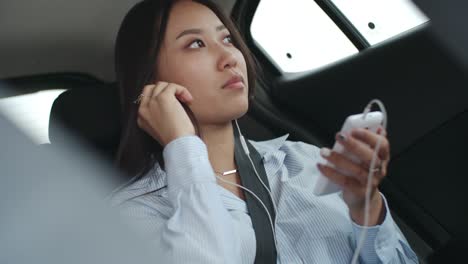 mujer asiática escuchando música en su teléfono inteligente en el coche