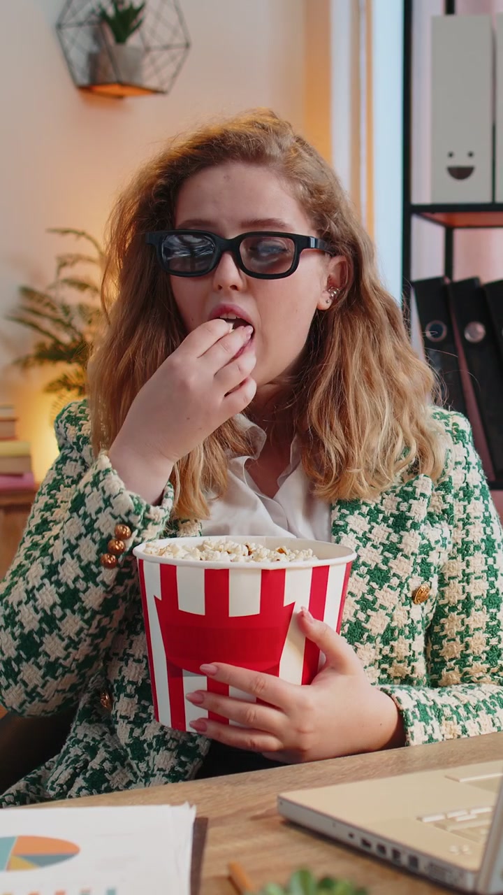 Donna d'affari che fa una pausa dal lavoro indossando occhiali 3D mangiando popcorn e guardando un film in ufficio