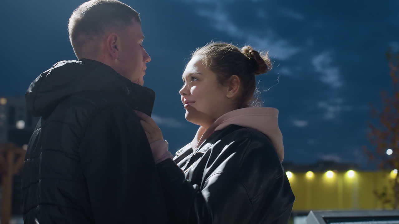 Lovely moment as man gently kisses wife on forehead during peaceful evening with smiles and closed eyes while soft city lights glow in background