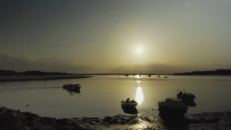 River-sunshine-in-the-morning-with-fishing-boat-passing-by-and-silhouette-boats-on-background-at-Tavira-Portugal