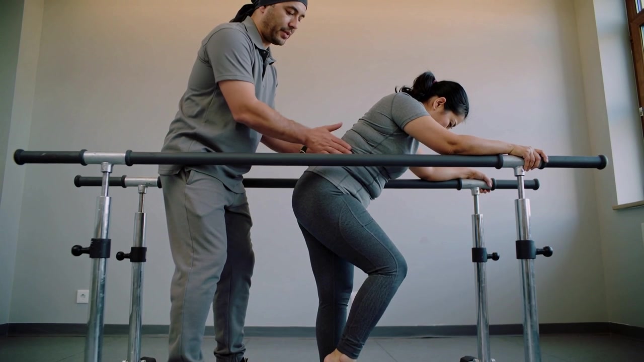 Stepping after therapist manual cueing, patient in gray activewear working on gait at parallel bars