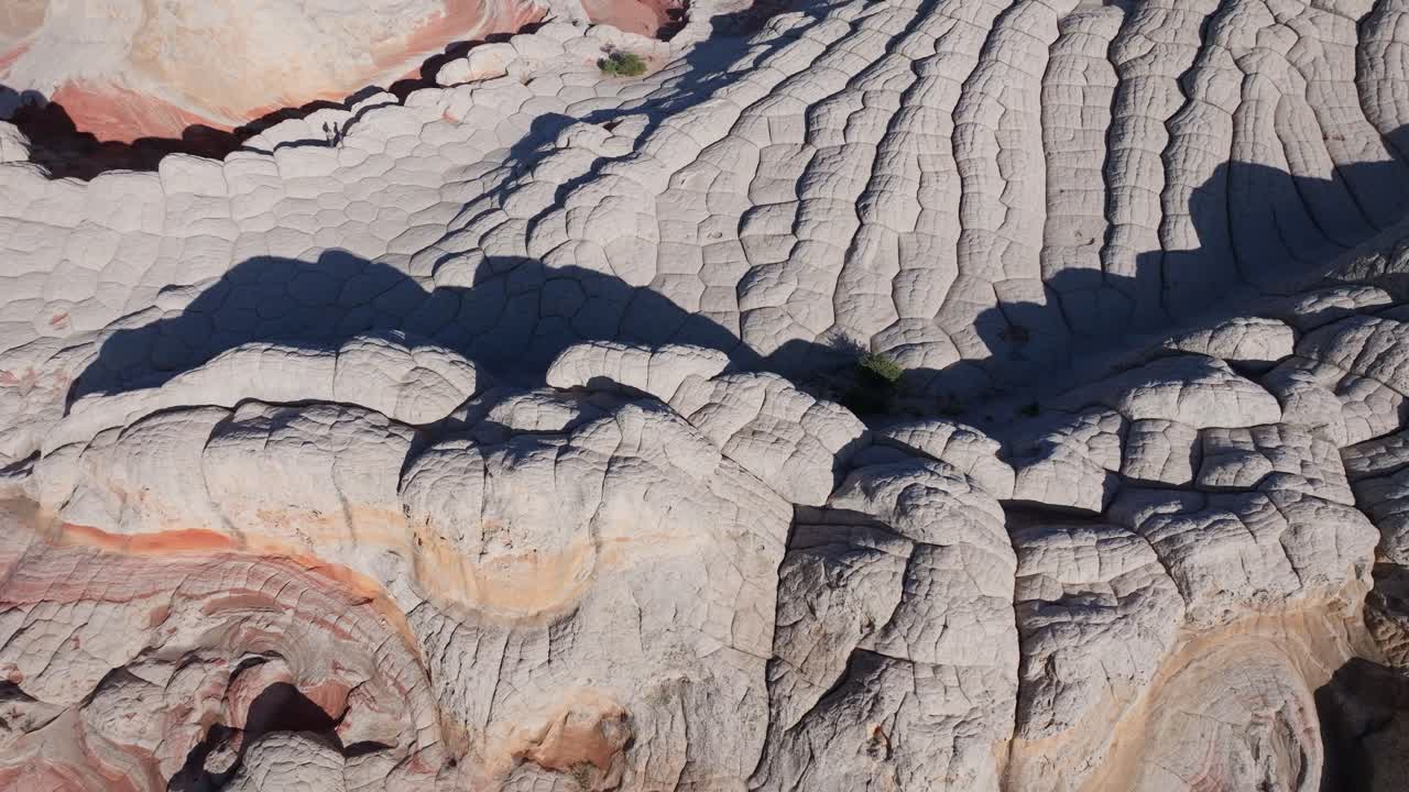 A drone shot circling the unique sandstone rock features of White Pocket Arizona surrounded by sandy desert and blue skies