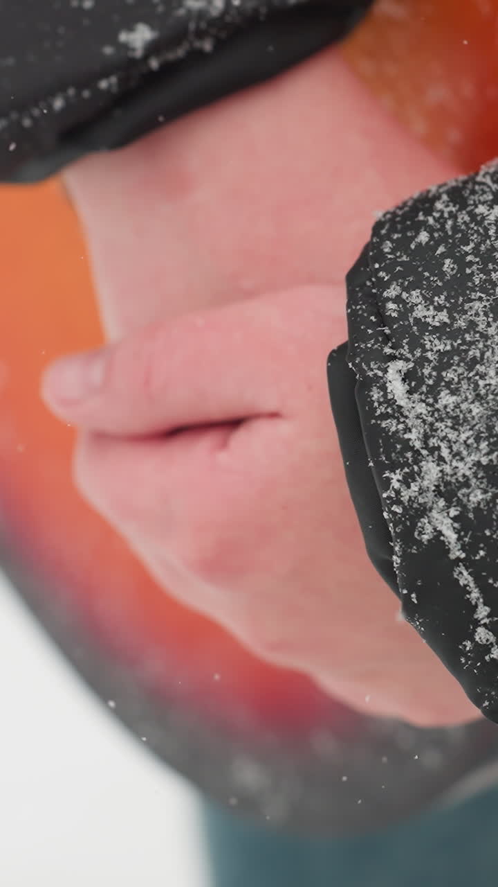 primer plano de manos sosteniendo una vibrante guitarra acústica roja en una escena de invierno nevado, con copos de nieve delicadamente descansando en la manga de la chaqueta negra