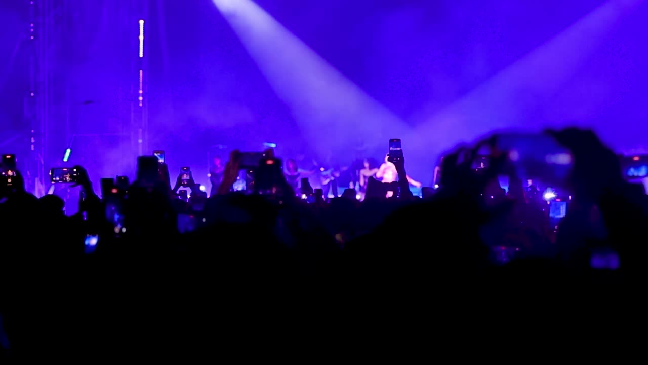 Una grande folla di fan che filma il palco con smartphone e trasmette in diretta il concerto.