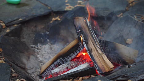 static fhd shot of logs slowly burning in a campsite fire, with red glowing embers in the center of the flames and rocks all around