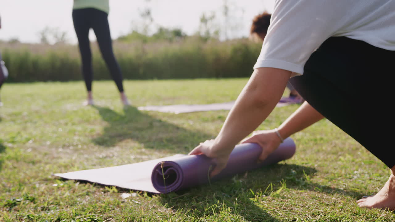amigas maduras enrollando esteras de ejercicio en la hierba al final de la lección de yoga al aire libre