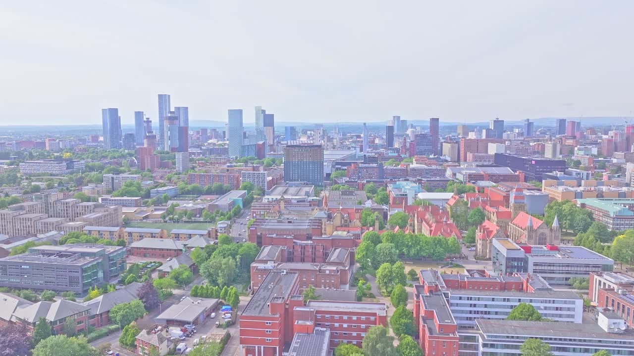 Slow aerial pan over Manchester from Dilworth Street reveals the University of Manchester campus and the modern skyline, including Beetham Tower and Deansgate Square, framed by green city blocks