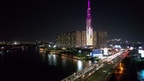 antena de coches y motos conduciendo sobre un puente con el edificio emblemático 81 en saigon vietnam por la noche