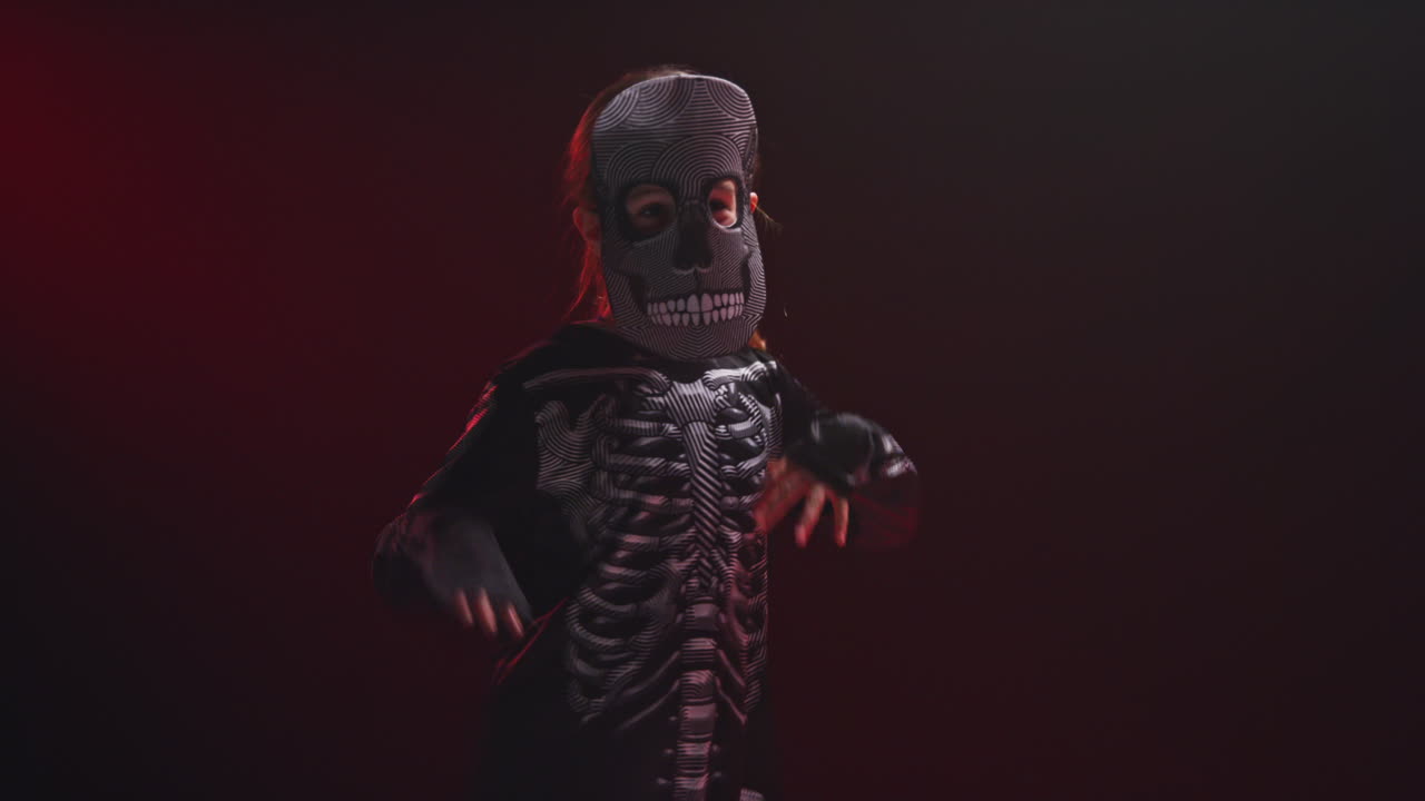 fotografía de estudio de un niño vestido con un disfraz de esqueleto haciendo un truco o un regalo en halloween bailando contra un fondo de humo rojo 10