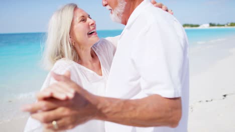 happy retired couple dancing together on tropical beach