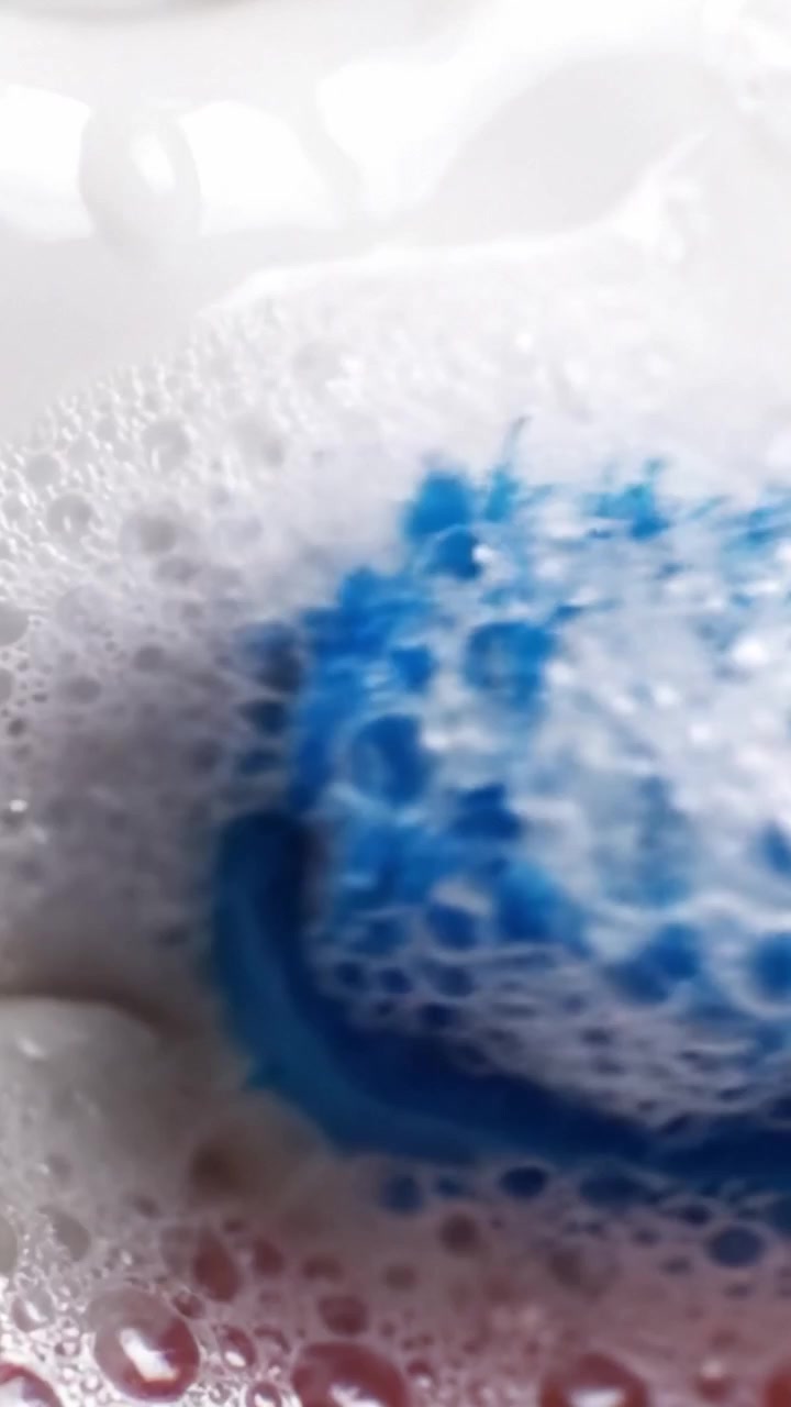 Primo Piano di Bolle e una Texture Simile a Panna Montata con un Pennello Blu che Crea Motivi e Forme Intricati su una Superficie Liscia