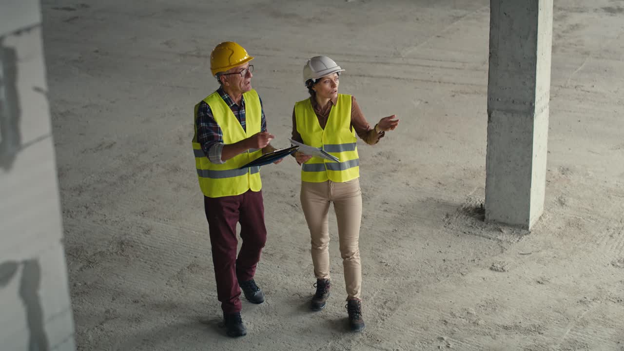 video de alto ángulo de ingenieros caucásicos masculinos y femeninos discutiendo y señalando en el sitio de construcción.