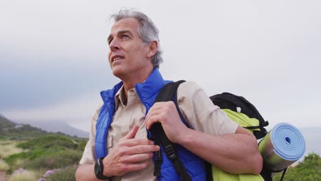 Senior-hiker-man-with-backpack-standing-and-looking-around-while-trekking-in-the-mountains.