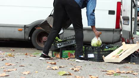 Vista-De-Cerca-De-Una-Mujer-Inmigrante-Negra-Buscando-Y-Recogiendo-Sobras-Después-De-Un-Mercado-Callejero-De-Comida-En-Milán,-Italia