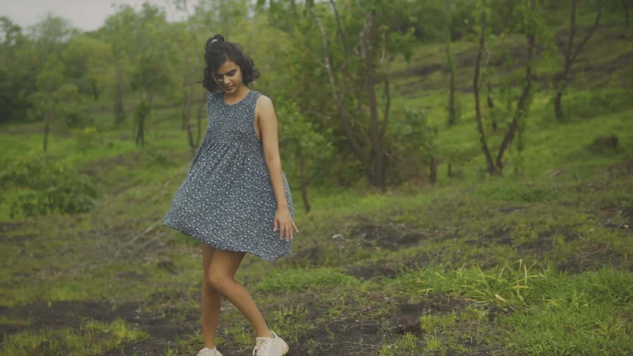mujer con vestido azul de pie en el campo abierto girando y caminando por el campo abierto