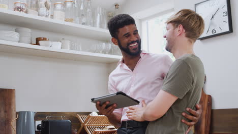 pareja gay usando tableta digital en casa en la cocina juntos
