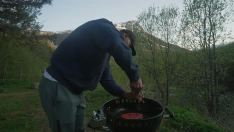 man seasoning fresh organic steak on grill in green outdoors with mountain backdrop