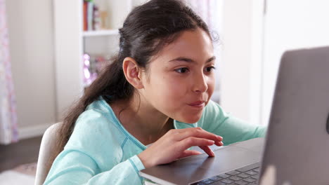 joven sentada en el escritorio en el dormitorio usando una computadora portátil