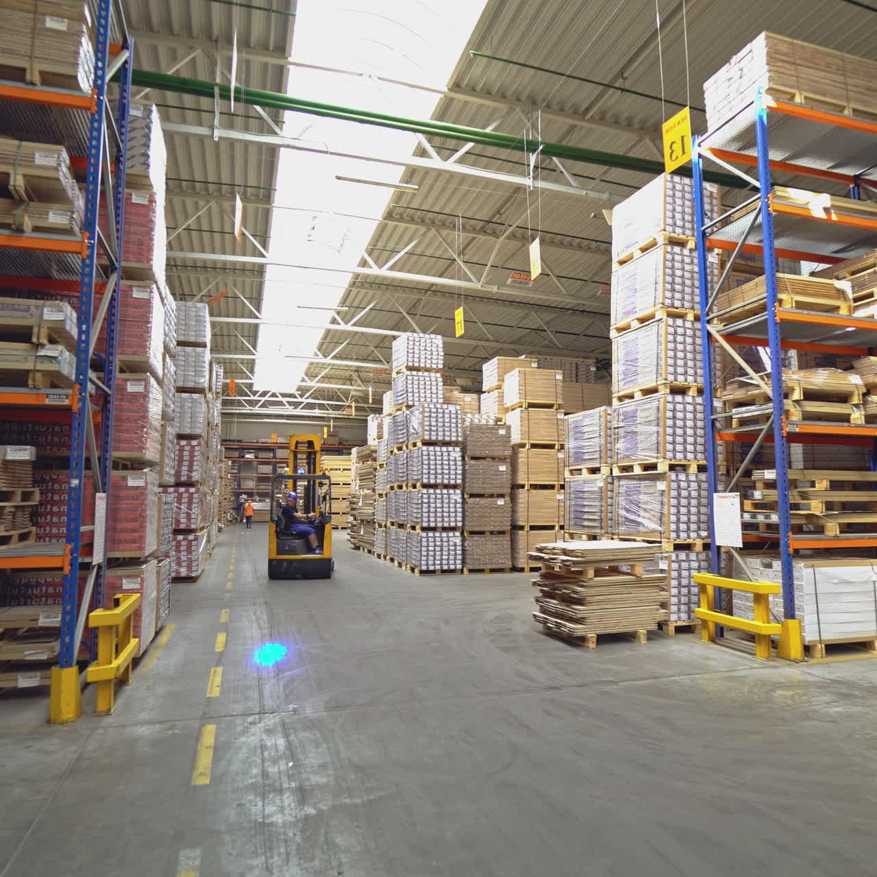 An orange electric stacker is driving between the shelves with goods in stock. Workflow in the company.