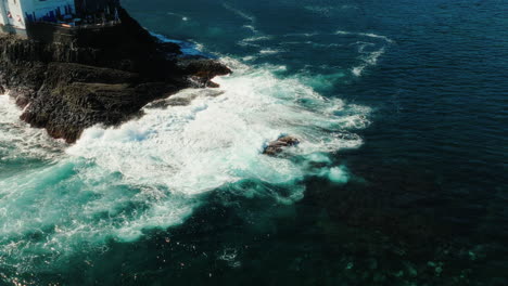 aerial: rocky spur in the atlantic ocean with waves crashing during the day in gran canaria, spain, establishing drone shot