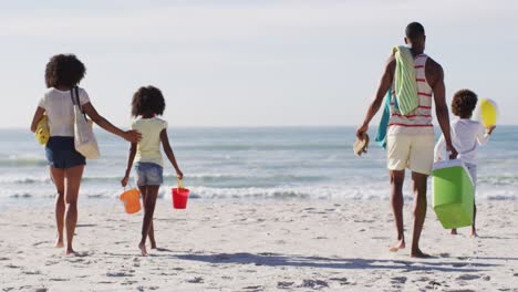 Padres-Afroamericanos-Y-Sus-Hijos-Sosteniendo-Equipos-De-Playa-En-La-Playa.