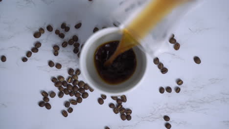 Hot-freshly-brewed-coffee-being-poured-into-white-mug-on-marble-table-with-beans-top-down