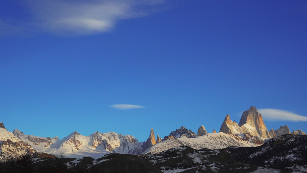 Montagne innevate all'alba sotto un cielo azzurro e limpido in una vista time-lapse da El Chaltén