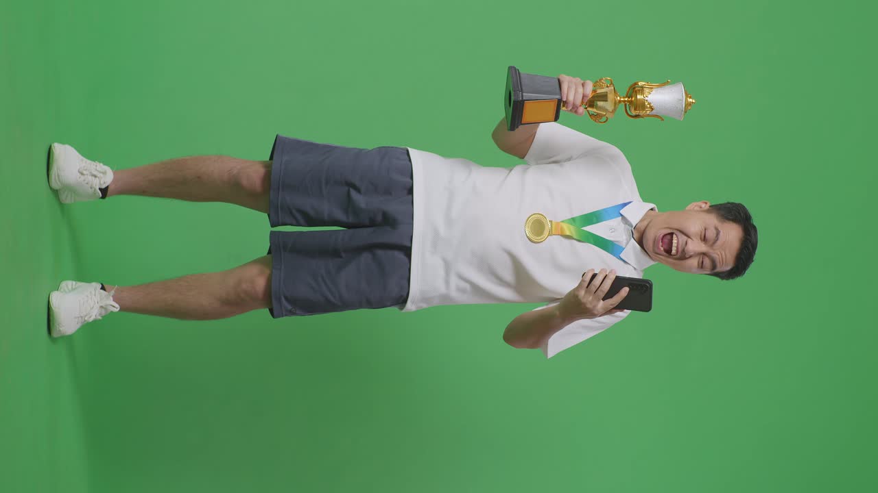 골드 메달과 트로피를 들고 스마트폰을 바라보는 아시아 남자의 몸이 가득 차 있고, 그 다음에는 스튜디오에서 녹색 화면 배경에서 축하하는 골을 비명을 지르고 있습니다.